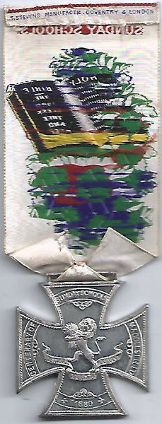 ribbon with words, image of bible and medal attached at pointed end